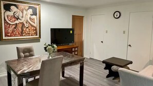 Un coin repas avec une table et des chaises, un téléviseur posé sur un meuble en bois et un tableau accroché au mur.