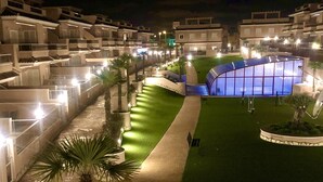 Un chemin bien éclairé mène à un grand bâtiment moderne doté d’une façade en verre incurvé.