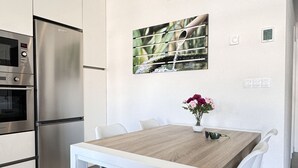 Une cuisine moderne avec des meubles blancs, un réfrigérateur en acier inoxydable et un coin repas comprenant une table en bois et des chaises blanches.