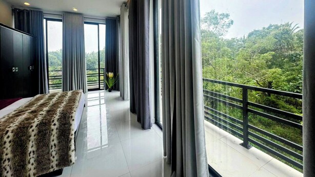 A modern hotel room with a large bed, a TV, and a balcony with a view of lush greenery.