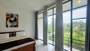 A modern bedroom with a large bed, a painting on the wall, and a balcony with a view of greenery.