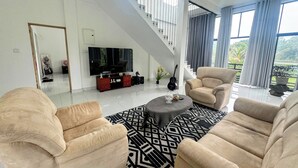 A spacious living room with a high ceiling, a staircase, a large flat-screen TV, and a view of the outdoors.