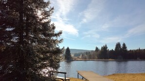 A lakeside bench area with a wooden platform extending into the water, surrounded by trees and a clear sky. - Gîte 'Les Ursules', sleeps 2 to 6 (Le Barboux)