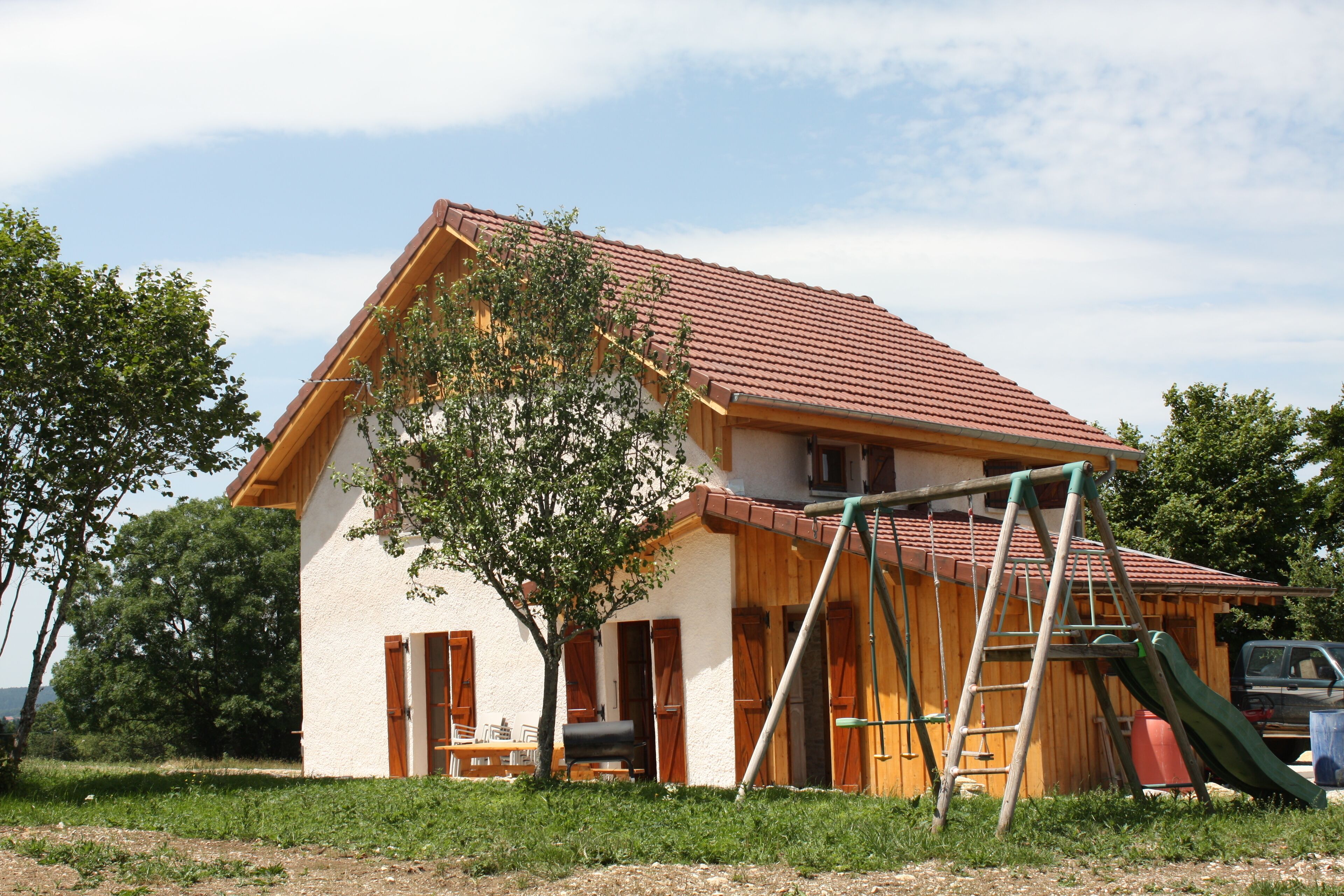 A house with a red-tiled roof, wooden exterior, and a swing set in the yard.