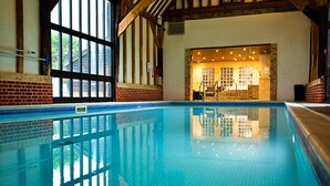 An indoor swimming pool with clear blue water, wooden beams, and a brick wall. - Lodge in Caldecott Hall with Private Hot Tub (Fritton)