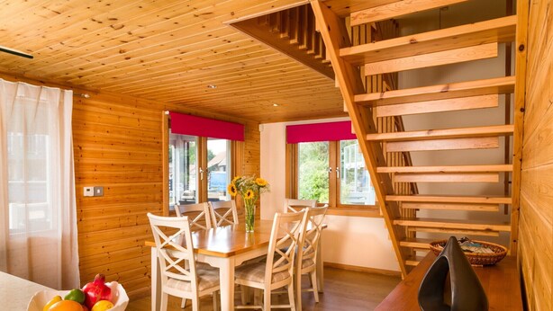 A wooden interior with a dining table, chairs, a fruit bowl, and a staircase. - Lodge in Caldecott Hall with Private Hot Tub (Fritton)