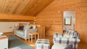 A cozy wooden interior with a high ceiling, a sofa, a plaid armchair, and a small table. - Lodge in Caldecott Hall with Private Hot Tub (Fritton)