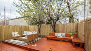 Eine Holzterrasse mit Gartenmöbeln, darunter eine Couch und Stühle, umgeben von einem Holzzaun.