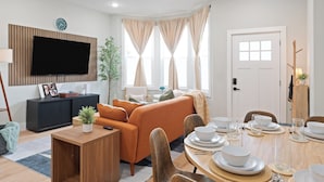 Ein modernes Wohnzimmer mit Sofa, Esstisch für vier Personen und einem an der Wand befestigten Flachbildfernseher.