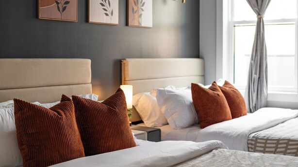 Ein Hotelzimmer mit Bett, Kissen, einem Nachttisch, einer Lampe und Wandbildern.
