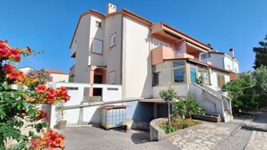 A multi-story building with a staircase leading to the entrance, surrounded by greenery and a paved area. - Apartman Štefica with AC and balcony for 2 people (Punat)
