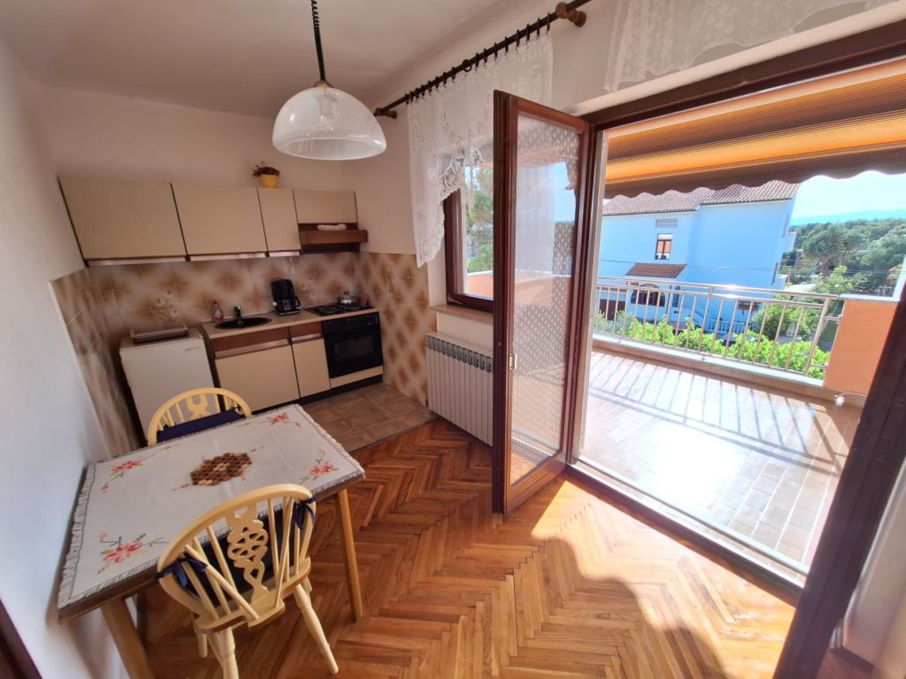Cocina compacta con zona de comedor, puerta corrediza de vidrio a un balcón y vista de un edificio azul.