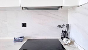 A kitchen with a black induction cooktop, white marble backsplash, and a utensil holder with kitchen tools. - PRAIA DA ROCHA - BELO HORIZONTE (Portimão)
