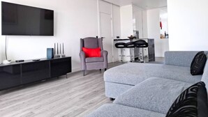A modern living room with a grey sofa, a red chair, a black entertainment unit, and a flat-screen TV mounted on the wall. - PRAIA DA ROCHA - BELO HORIZONTE (Portimão)