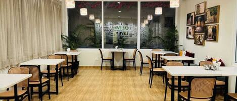 A dining area with tables and chairs, large windows with decorative elements, and hanging pendant lights.