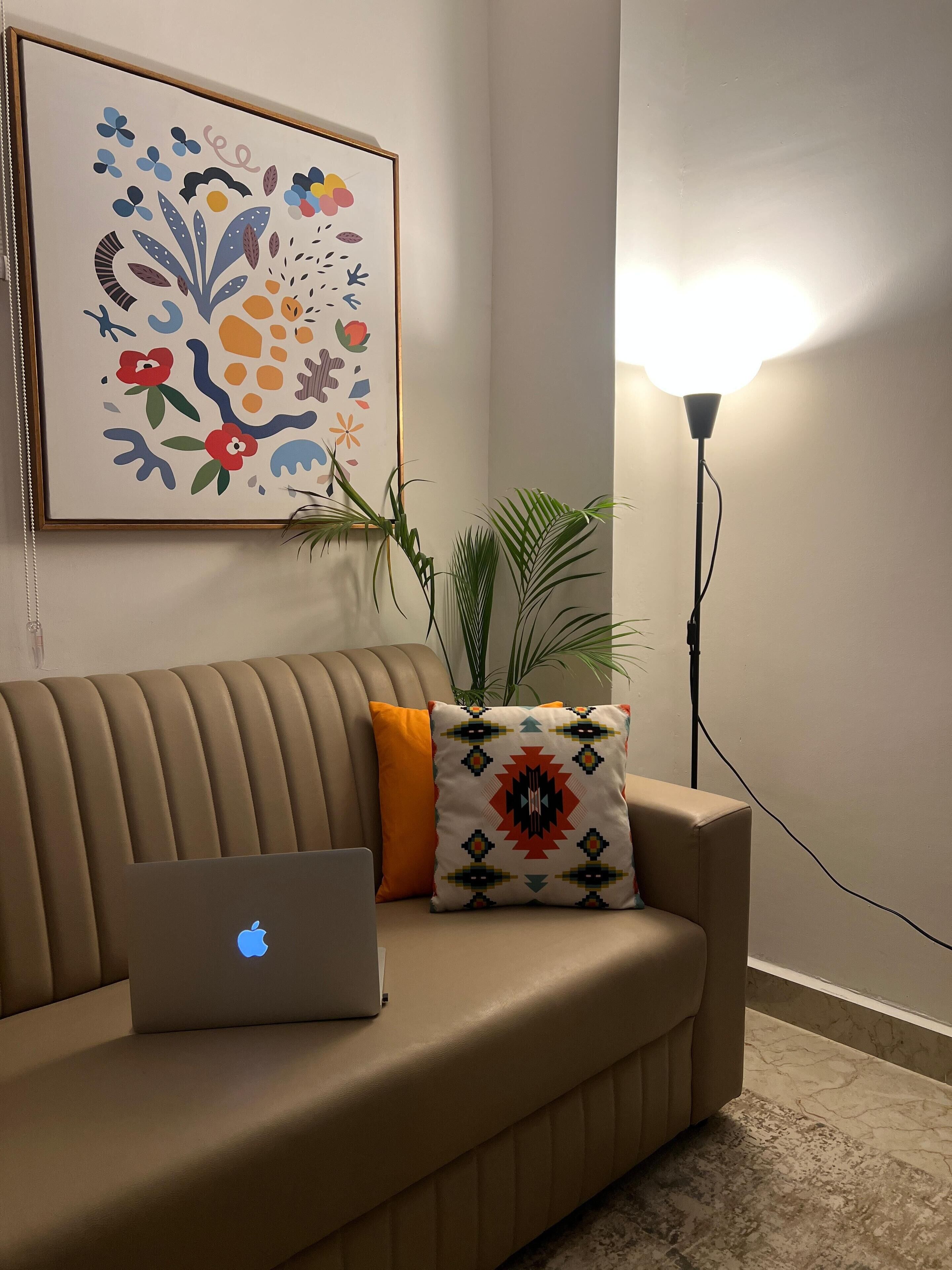 Un sofá beige con una laptop, un cojín colorido y una planta.