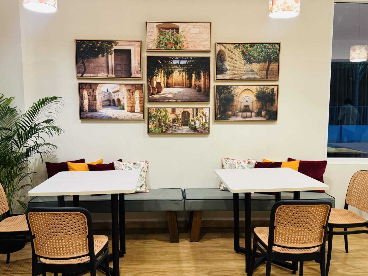 Un comedor con mesas y sillas, una planta grande en maceta, y seis cuadros en la pared.