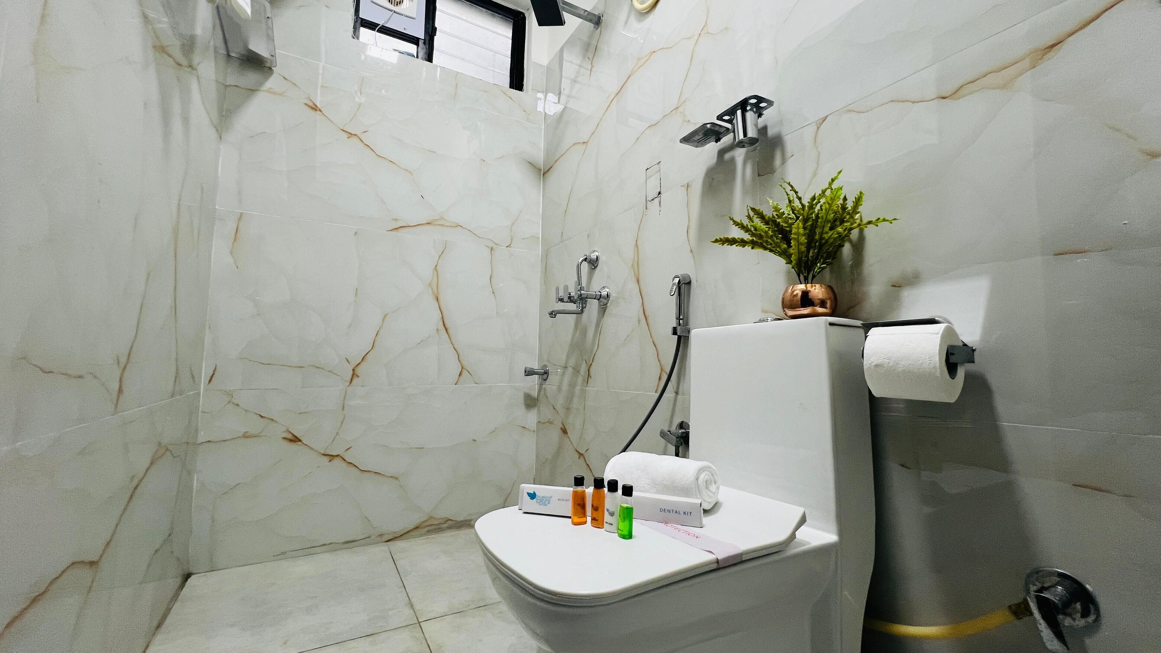 Ein Badezimmer mit Marmorwand, Toilette, Dusche und einer kleinen Pflanze an der Wand.