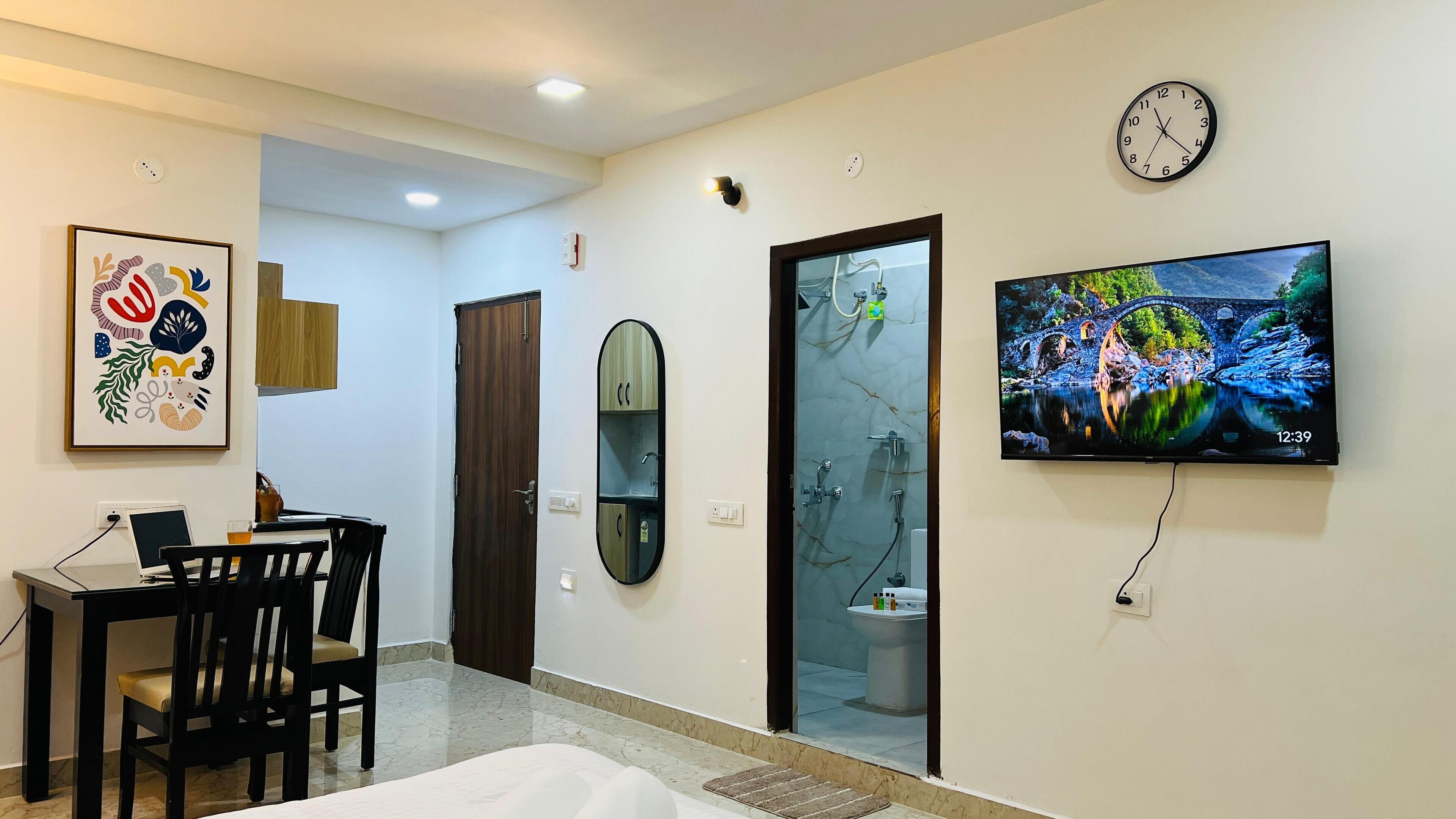 A modern living room with a TV, a dining area with a laptop, a wooden door, and a wall-mounted clock.