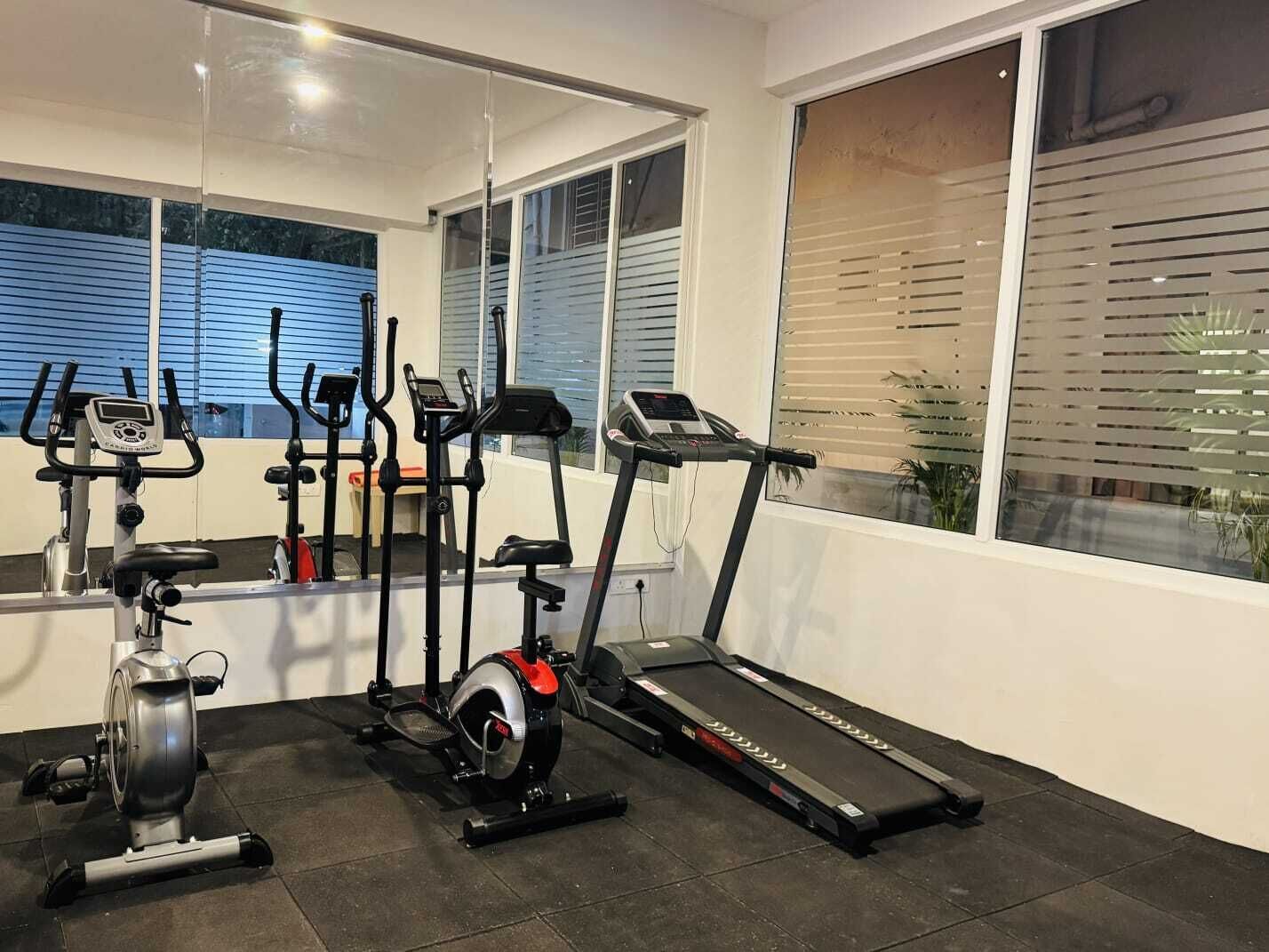 A home gym with exercise equipment including a stationary bike, elliptical, treadmill, and weights.