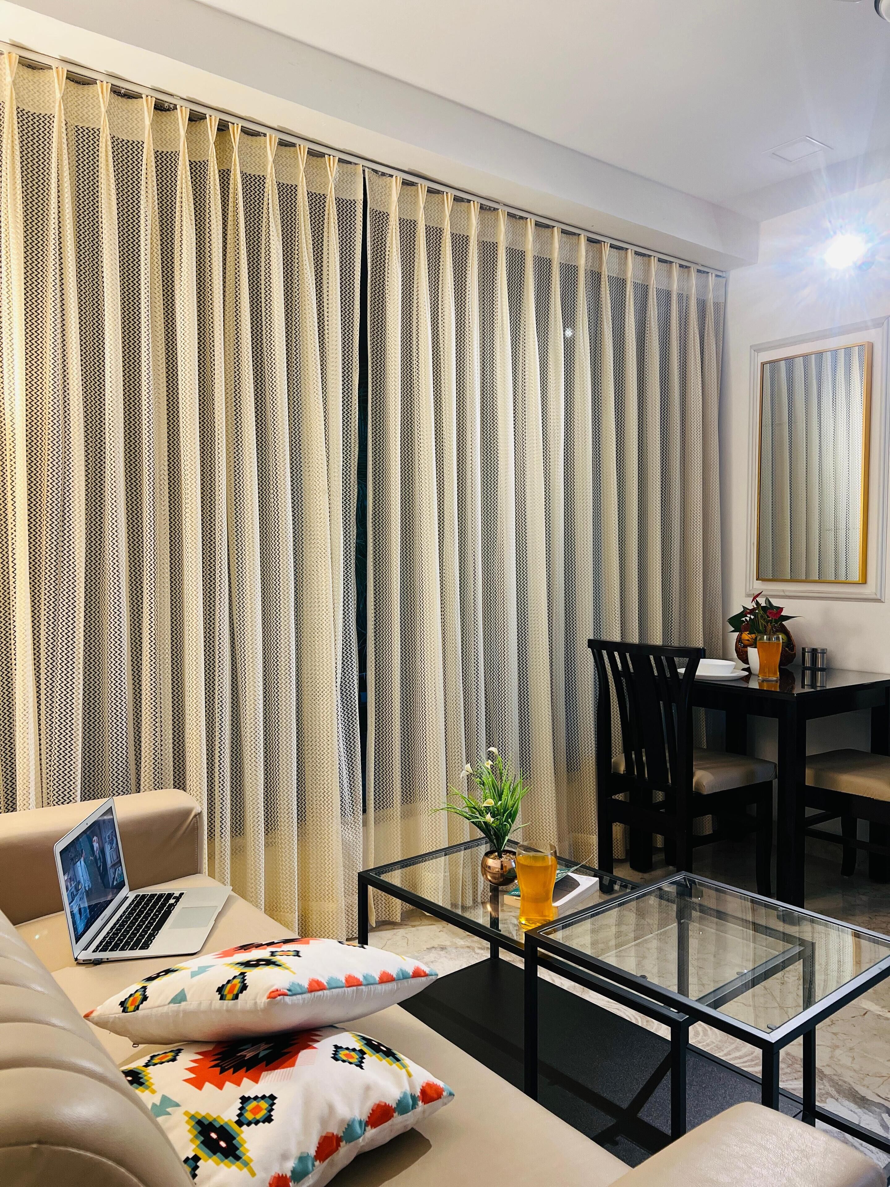 A modern living room with a sofa, a glass coffee table, a laptop, and a dining area with a table and chairs.
