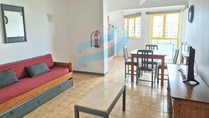 Uma sala de estar com um sofá vermelho, uma mesa de centro de madeira e um espaço de jantar com cadeiras e uma mesa.