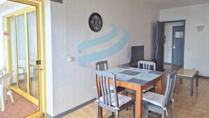 Uma área de refeições com mesa e cadeiras, um relógio na parede e uma porta que dá para uma varanda.