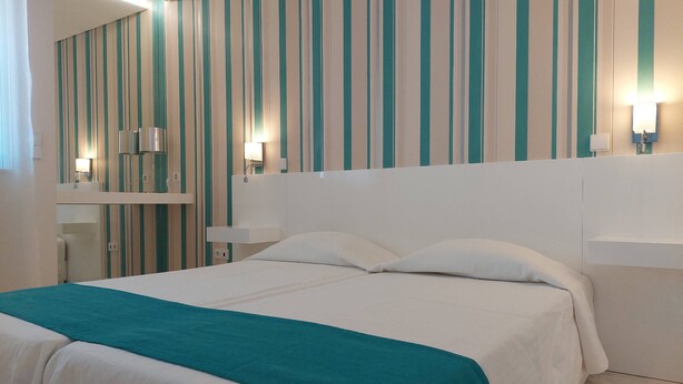 Ein Hotelzimmer mit einem Bett, einem Nachttisch, einem Spiegel und einer gestreiften Wand.