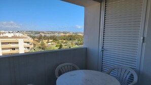 Ein Balkon mit rundem Tisch und zwei Stühlen, der auf einen Wohnbereich mit Gebäuden und Grünflächen blickt.