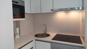 Eine moderne Küche mit weißen Schränken, einer Edelstahlspüle, einem Backofen und einem Kochfeld.