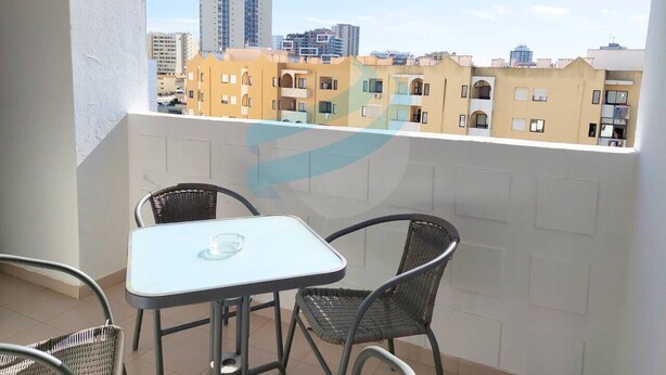 A balcony with a table and chairs, overlooking a cityscape with multi-story buildings. - PRAIA DA ROCHA – CLUB PRAIA DA ROCHA VI (Portimão)