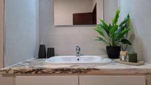 A bathroom with a marble countertop, a white sink, a mirror, a potted plant, and a small shelf with toiletries. - PRAIA DA ROCHA – CLUB PRAIA DA ROCHA VI (Portimão)