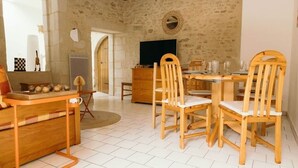 A dining area with a stone wall, wooden furniture, and a television. - La Belle Tuffière (Montreuil-Bellay)