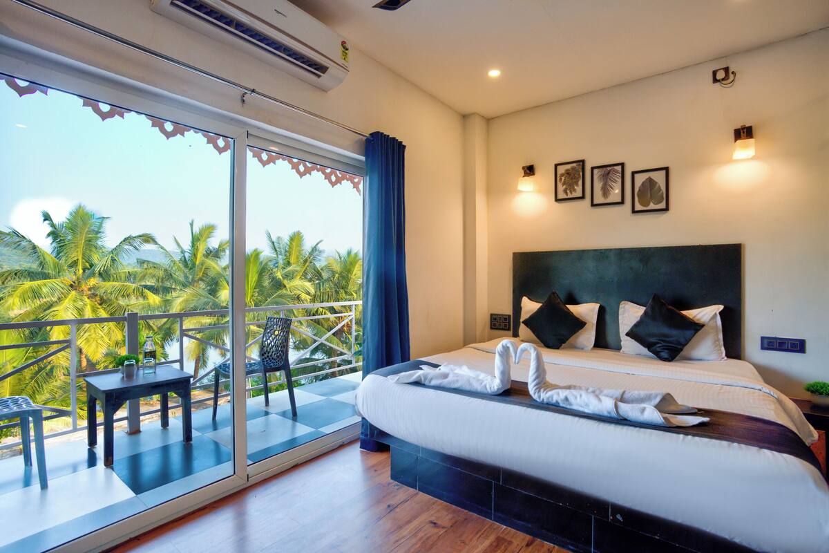 A hotel room with a balcony, a bed with white linens, and a view of palm trees.