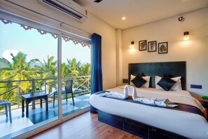 A hotel room with a balcony, a bed with white linens, and a view of palm trees. - Hotel Vaggi's Place (Arpora)