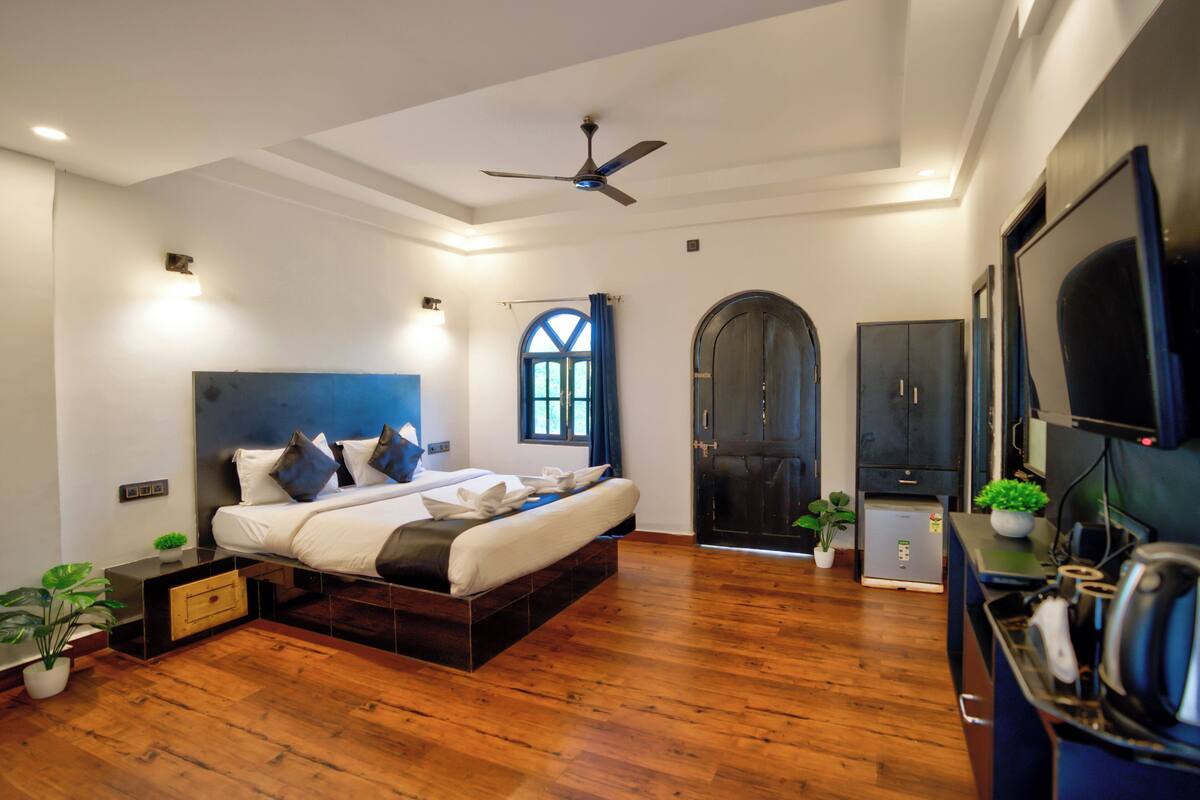 A bedroom with a bed, wooden floor, ceiling fan, TV, and a wardrobe.