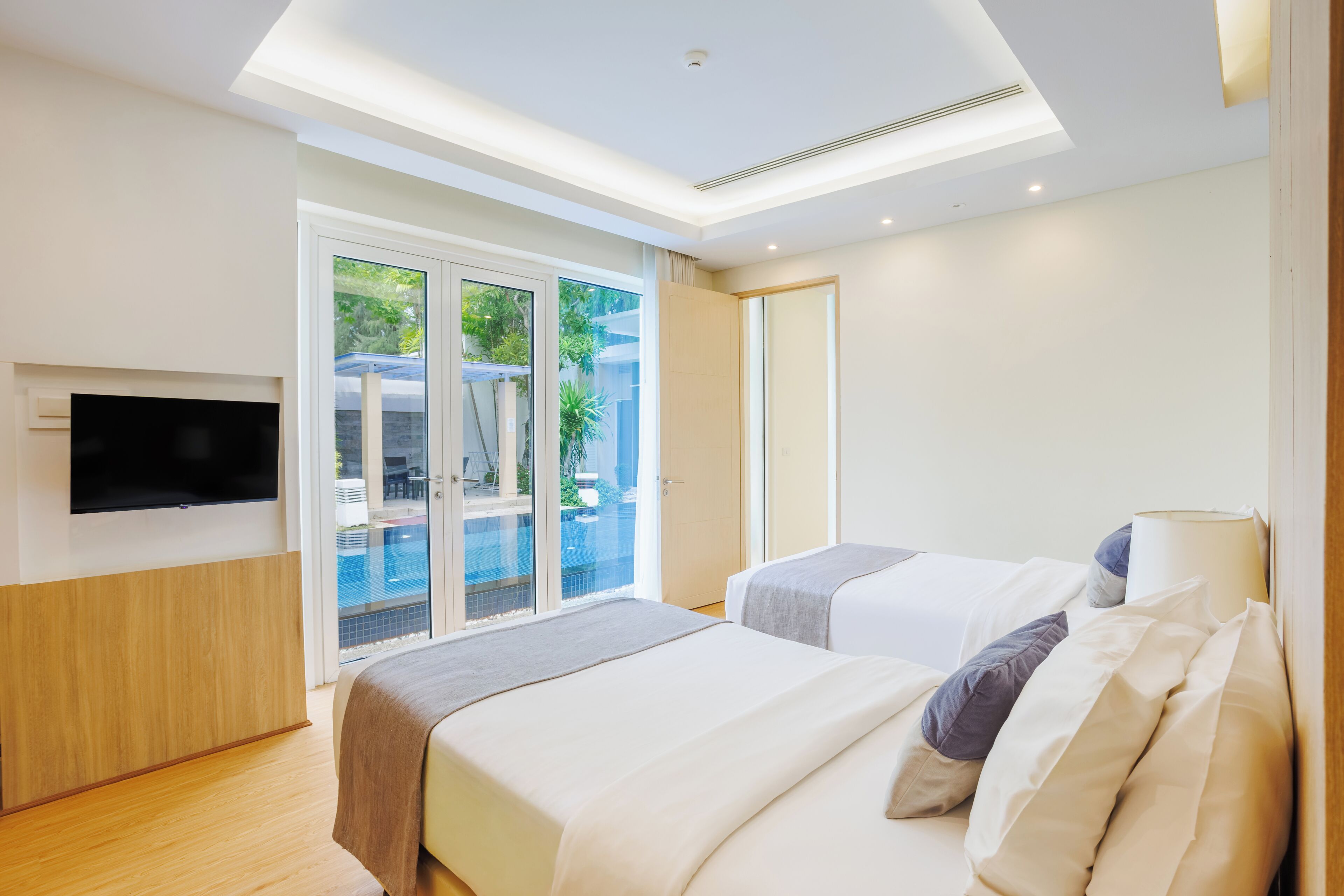 A hotel room with two beds, a flat-screen TV, and a sliding glass door leading to an outdoor area.