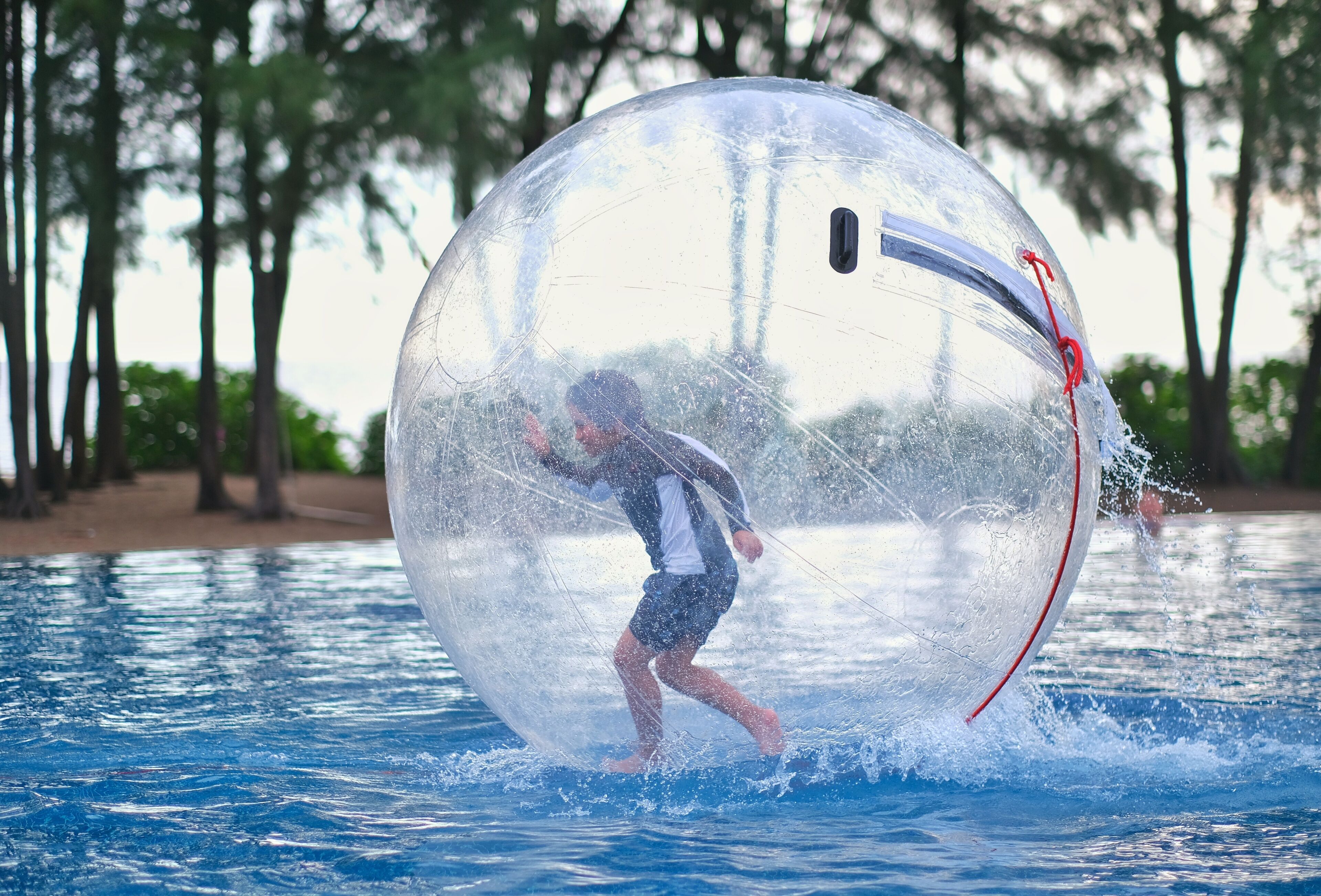 A person inside a transparent ball on water, with trees in the background.