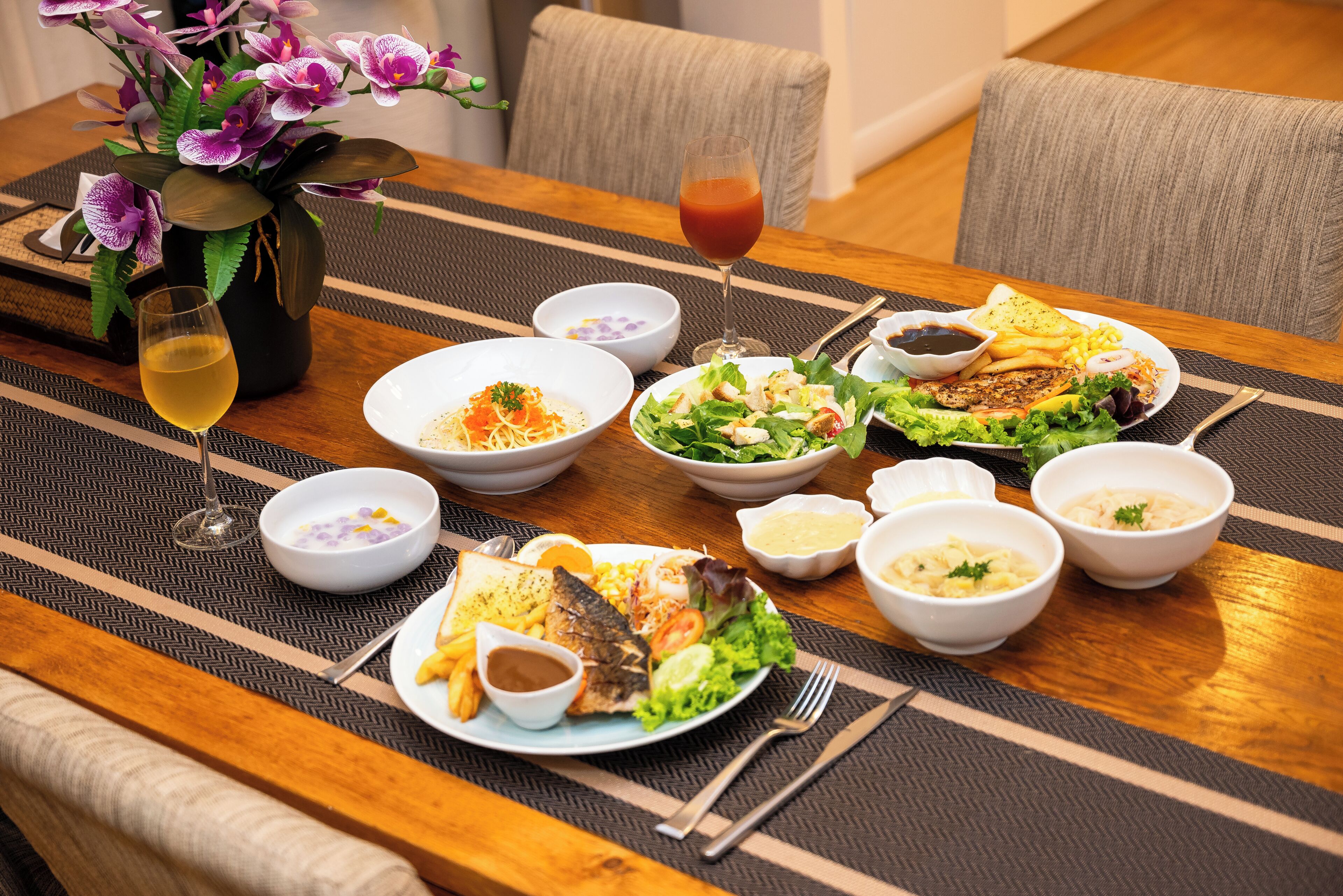 A dining table with various dishes, including fish, salad, and bread, along with drinks and small bowls of sauces.