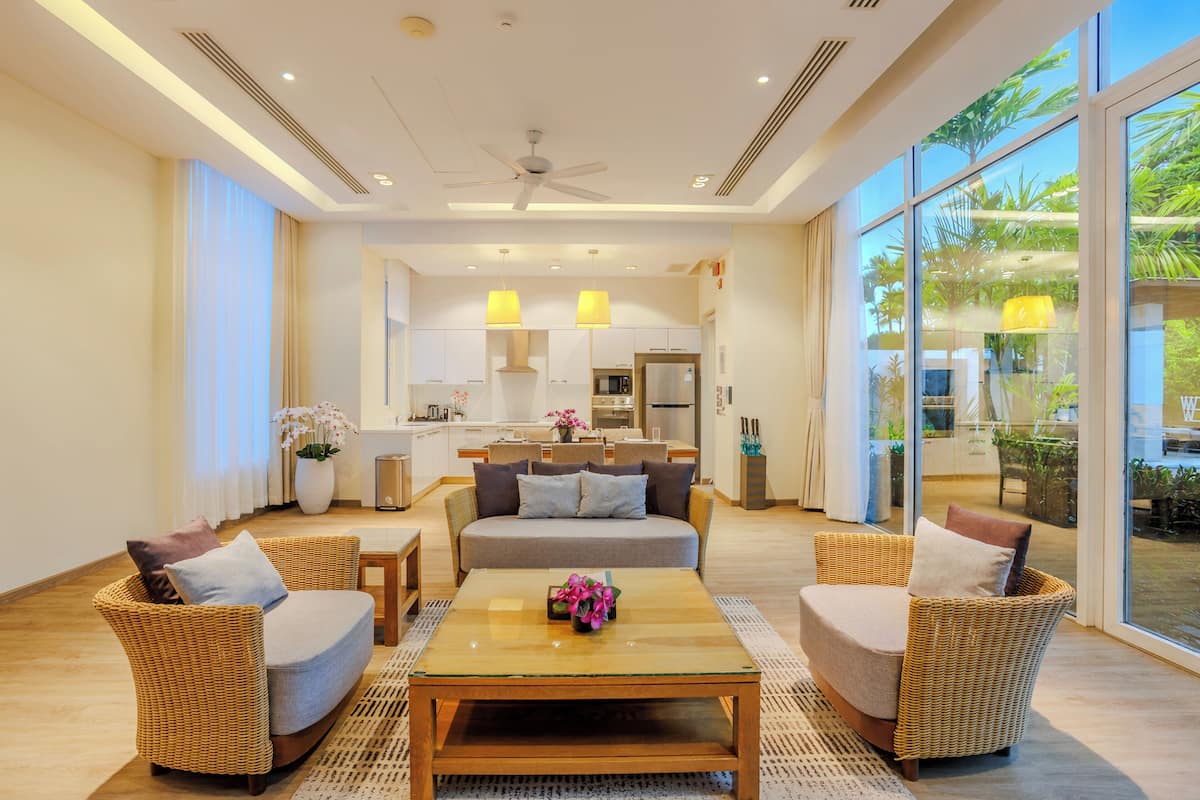 A modern living room with a sofa, two armchairs, a coffee table, and a kitchen in the background.