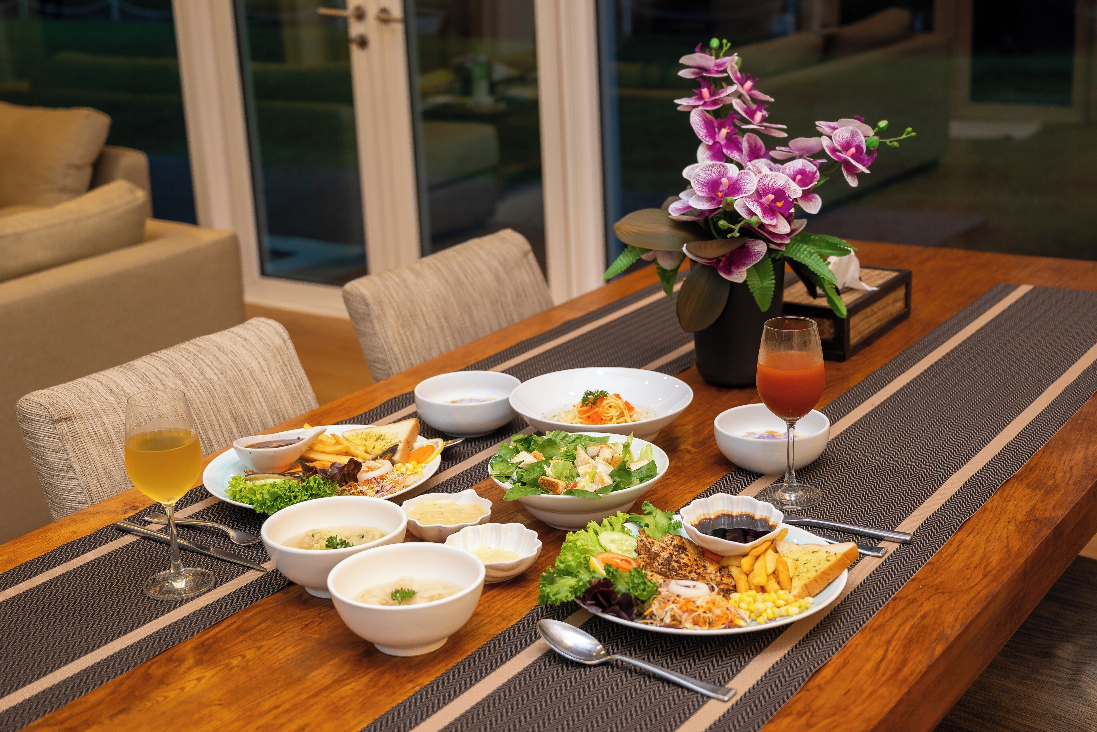 Une table à manger avec différents plats, un verre de vin et un vase de fleurs.