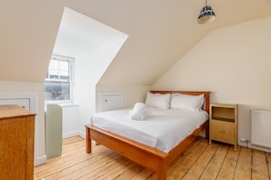 A bedroom with a wooden bed, white linens, a nightstand, a dresser, and a window with a view. - Market Street (No 97) (St Andrews)