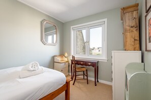 A bedroom with a bed, a desk, a chair, a wardrobe, and a window with a view. - Market Street (No 97) (St Andrews)