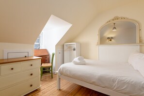 A bedroom with a sloped ceiling, a bed, a dresser, a chair, and a wardrobe. - Market Street (No 97) (St Andrews)