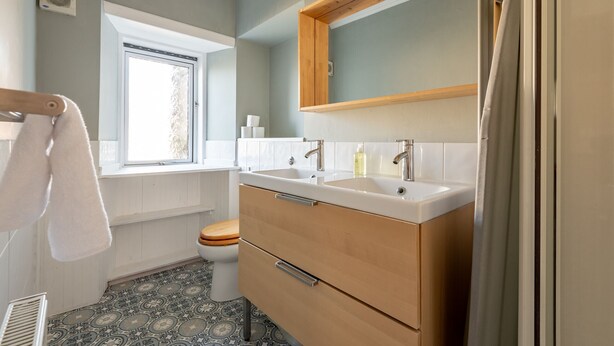 Une salle de bain avec une fenêtre, deux lavabos, des toilettes et des carreaux de sol à motifs.