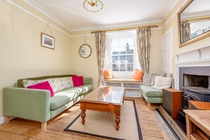 A living room with a green sofa, a wooden coffee table, a fireplace, and a window with curtains. - Market Street (No 97) (St Andrews)
