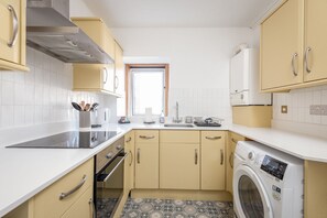 Une cuisine compacte avec des meubles de couleur beige, un four encastré, un lave-linge et une fenêtre qui laisse entrer la lumière naturelle.