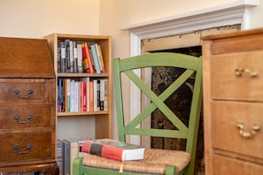 A room with a wooden dresser, a green chair, and a bookshelf filled with books. - Market Street (No 97) (St Andrews)