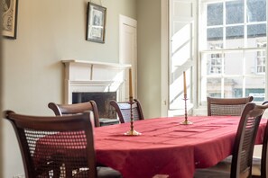 A dining room with a red tablecloth, wooden chairs, a fireplace, and a large window. - Market Street (No 97) (St Andrews)
