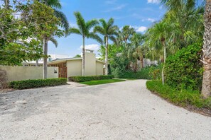 A residential property with a gravel driveway, palm trees, and a house with a beige exterior.